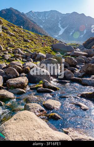 Un ruisseau de montagne clair coule sur des rochers moussus avec une chaîne de montagnes himalayenne dramatique en arrière-plan. Banque D'Images