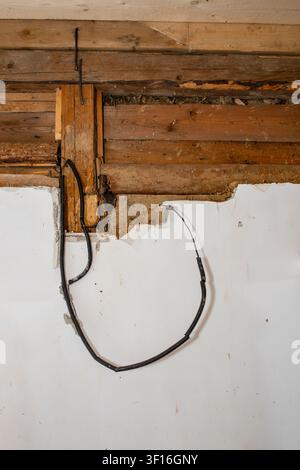 Câblage électrique exposé dans un conduit flexible suspendu à un vieux mur en rondins Banque D'Images