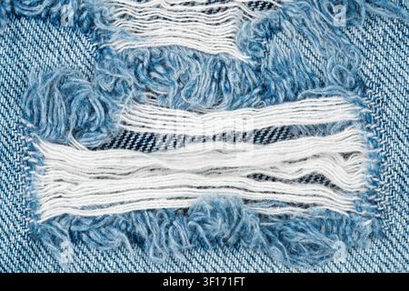 Close-up d'un denim bleu déchiré avec des bords effilochés et des fils blancs apparents. Surface texturée du tissu, éclairage naturel, style décontracté. Idéal pour la mode Banque D'Images