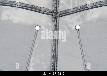Vue macro du tissu denim gris avec texture visible, rivets métalliques, coutures renforcées. Tons neutres, éclairage uniforme, composition minimale. Idéal pour Banque D'Images