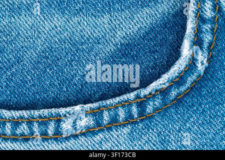 Détail macro du tissu bleu denim classique. Texture usée avec bordure de poche avant effilochée et surpiqûre orange contrastée créant un fond simple et décontracté Banque D'Images