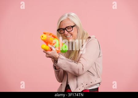 Sénior jouant avec un pistolet à eau et profitant d'une maturité active Banque D'Images
