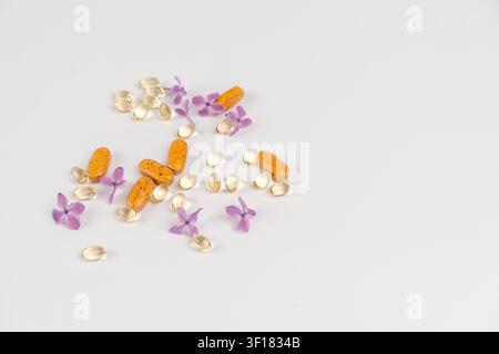 Différentes capsules de vitamines sont posées sur une surface plane avec de petites pétales de fleurs. L'image montre un mélange de couleurs et de formes dans un espace bien éclairé. Banque D'Images