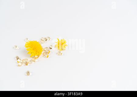 Des fleurs jaunes sont placées près de capsules de vitamine transparentes sur une surface blanche unie. La scène montre un arrangement simple qui met en évidence un allergène potentiel Banque D'Images