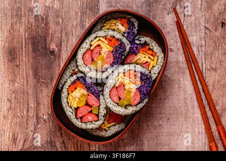 Kimbap (ou gimbap) coloré avec des légumes et de la saucisse dans une boîte en bois sur une surface en bois Banque D'Images