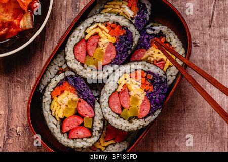 Kimbap (ou gimbap) coloré avec des légumes et de la saucisse dans une boîte en bois sur une surface en bois Banque D'Images