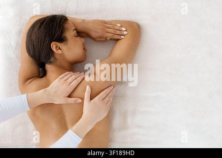 Jeune femme noire recevant un massage doux des épaules et du dos sur un lit de spa Banque D'Images