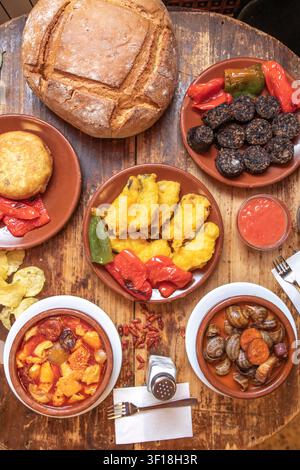 Présentoir de tapas espagnoles traditionnelles avec pain rustique, poivrons frits, saucisse de sang, escargots et ragoût de tripes sur table en bois Banque D'Images