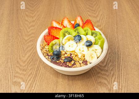 Bol Acai garni de fraises tranchées, kiwi, banane, myrtilles et granola sur table en bois Banque D'Images