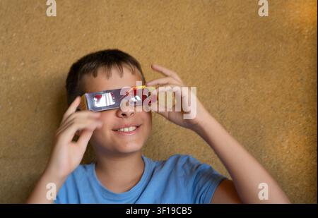 Un garçon souriant tout en portant des lunettes spéciales pour observer en toute sécurité une éclipse solaire. Banque D'Images