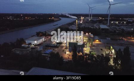 Vue nocturne d'une zone industrielle illuminée près d'une rivière, avec des éoliennes en arrière-plan, Allemagne Banque D'Images