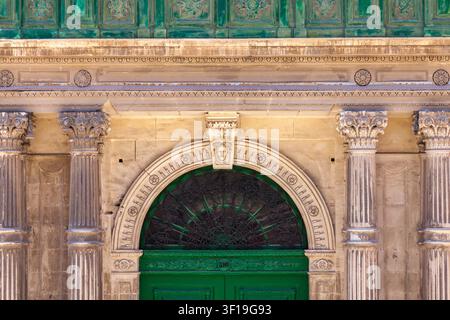 Détail rapproché d'une porte verte cintrée ornée avec un fanal en fer forgé complexe, encadrée par des colonnes sculptées à La Valette, Malte Banque D'Images