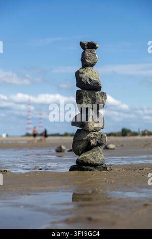Cairn de pierres équilibré se dressant sur une plage de sable à marée basse devant un ciel bleu, symbole d'équilibre et de pleine conscience Banque D'Images