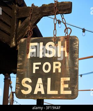 Un panneau en bois rustique usé portant l'inscription "Fish For Sale" suspendu à des chaînes rouillées au port de Southwold, Suffolk, Angleterre. Banque D'Images