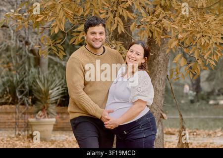 Moment de maternité chaud en extérieur sous les feuilles d'automne, mettant en scène un couple aimant étreignant le ventre rond, idéal pour la famille, la parentalité, la grossesse, le style de vie Banque D'Images
