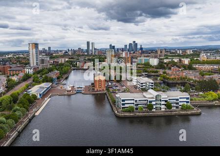 Vue aérienne de la zone riveraine de Salford Quays présentant des bâtiments de bureaux modernes, des eaux de canal calmes et la ligne d'horizon de la ville de Manchester sous un ciel nuageux Banque D'Images