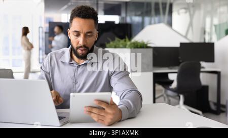 Homme d'affaires travaillant en ligne à l'aide d'une tablette numérique et d'un ordinateur portable sur son lieu de travail Banque D'Images