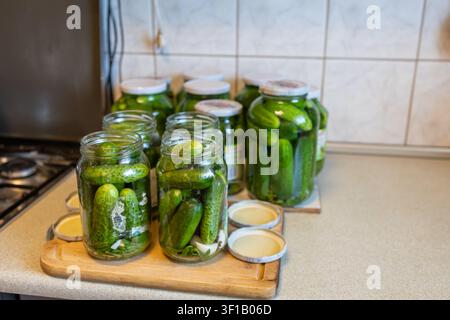 Plusieurs bocaux remplis de concombres attendant d'être scellés pendant la conservation maison sur un comptoir de cuisine lumineux. Banque D'Images