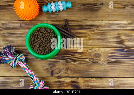 Jouets pour chiens et aliments pour chiens dans un bol en plastique vert sur fond en bois. Vue de dessus. Concept de soins pour chiens Banque D'Images