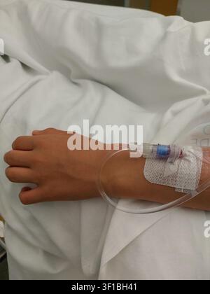 Une vue détaillée d'une ligne IV médicale et d'un cathéter fixés sur une main d'enfant reposant dans un lit de clinique, représentant les soins de santé pédiatriques, l'insuffisance médicale Banque D'Images