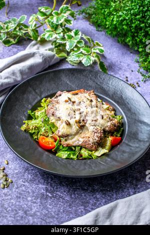 Steak grillé style restaurant avec fromage fondu crémeux servi avec une salade de légumes verts mélangés Banque D'Images