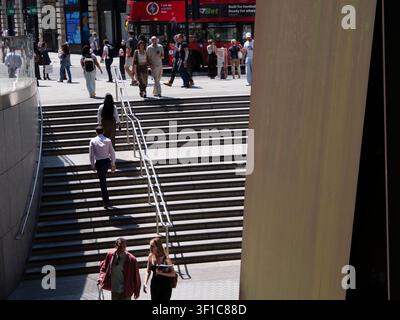 Des acheteurs et des navetteurs descendent une large volée d'escaliers extérieurs menant aux places d'entreprises modernes du domaine de Broadgate dans la City de Londres, au Royaume-Uni, encadrés à droite par Fulcrum, une sculpture monumentale en tôle d'acier patiné spécifique au site de l'acclamé artiste contemporain américain Richard Serra Banque D'Images