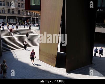 Des acheteurs et des navetteurs descendent une large volée d'escaliers extérieurs menant aux places d'entreprises modernes du domaine de Broadgate dans la City de Londres, au Royaume-Uni, encadrés à droite par Fulcrum, une sculpture monumentale en tôle d'acier patiné spécifique au site de l'acclamé artiste contemporain américain Richard Serra Banque D'Images