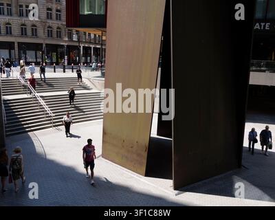 Des acheteurs et des navetteurs descendent une large volée d'escaliers extérieurs menant aux places d'entreprises modernes du domaine de Broadgate dans la City de Londres, au Royaume-Uni, encadrés à droite par Fulcrum, une sculpture monumentale en tôle d'acier patiné spécifique au site de l'acclamé artiste contemporain américain Richard Serra Banque D'Images