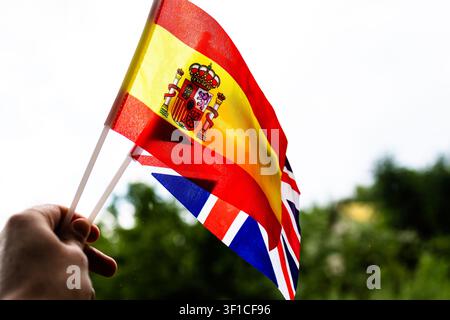 Une main brandissant haut les drapeaux de l'Espagne et du Royaume-Uni avec la lumière du soleil traversant le tissu, suggérant une culture partagée, un apprentissage des langues, une fierté sportive et une attitude accueillante Banque D'Images