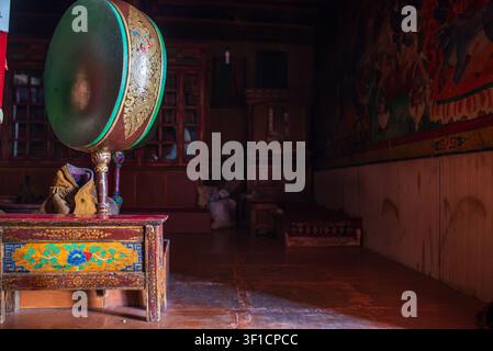 Intérieur faiblement éclairé d'un monastère bouddhiste. À gauche se trouve un grand tambour rituel chöd monté sur une armoire en bois finement sculptée avec des f colorés Banque D'Images