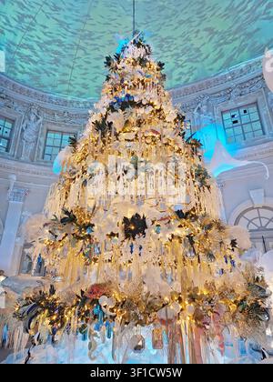 Maincy, France – 11 décembre 2025 : Un immense sapin de Noël dans une grande salle, décoré selon un thème aquatique unique, avec des ornements dorés et blancs en Banque D'Images