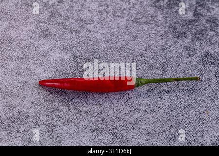 Piment rouge vif avec tige verte centré sur un fond gris moucheté. Composition minimaliste avec un éclairage doux mettant en valeur le ski brillant du piment Banque D'Images