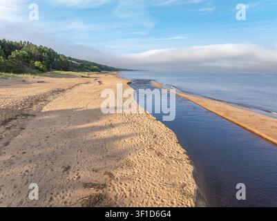 Vue aérienne de l'embouchure de la rivière Peterupe se déversant dans la mer Baltique près de Saulkrasti, en Lettonie, à un lever de soleil doré Banque D'Images