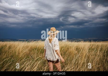 Météo en été. Femme avec chapeau de paille anticipant une tempête et observant des nuages dramatiques sur la campagne Banque D'Images