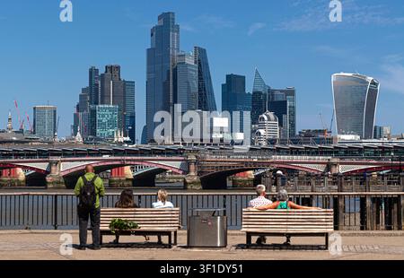 Personnes assises sur des bancs contemplant la skyline de Londres, South Bank Londres, Angleterre, Royaume-Uni. Banque D'Images