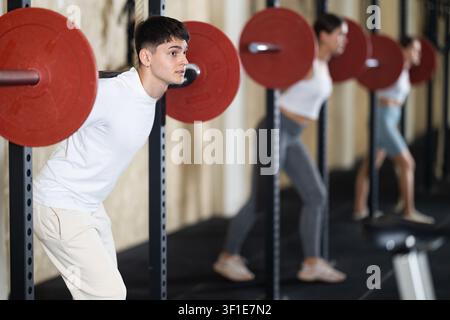 Jeune homme faisant des exercices avec une barre dans le gymnase Banque D'Images