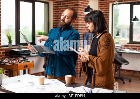 Homme d'affaires présente des statistiques marketing sur un ordinateur portable lors d'un moment de bureau impliquant un mur de briques, un ordinateur portable d'homme d'affaires et un ordinateur portable Banque D'Images