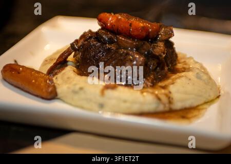 Une photographie de style restaurant en gros plan de côtes de bœuf braisées ou rôti de bœuf savoureux, garnies de carottes baby glacées et d'une sauce riche, reposant sur un Be Banque D'Images
