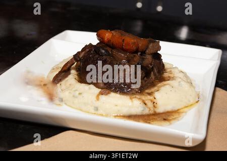 Une photographie de style restaurant en gros plan de côtes de bœuf braisées ou rôti de bœuf savoureux, garnies de carottes baby glacées et d'une sauce riche, reposant sur un Be Banque D'Images