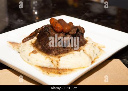 Une photographie de style restaurant en gros plan de côtes de bœuf braisées ou rôti de bœuf savoureux, garnies de carottes baby glacées et d'une sauce riche, reposant sur un Be Banque D'Images