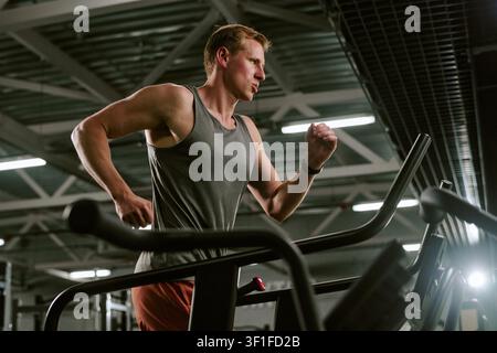 Homme athlétique courant sur un tapis roulant pendant un entraînement cardio en salle de sport Banque D'Images