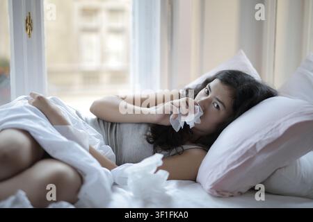Jeune femme malade allongée dans son lit avec un mouchoir Banque D'Images