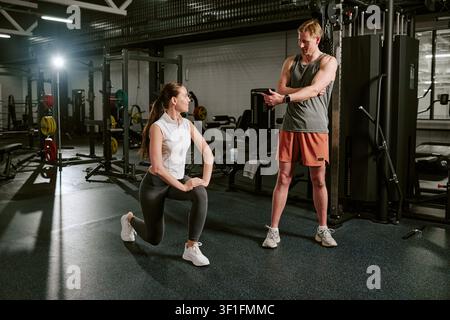 Jeune femme faisant de l'exercice avec un entraîneur masculin dans une salle de sport pour la forme physique Banque D'Images