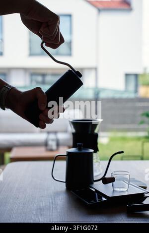 Silhouette d'une personne moulant des grains de café avec une moulin à main à côté d'outils de café en infusion près d'une fenêtre. Concept de café frais, de brassage à la main et de routine matinale. Banque D'Images