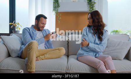 Femme caucasienne mécontente et agacée, offensée, regardant un homme occupé avec son téléphone portable, accro aux gadgets, riant en regardant une vidéo humoristique, riant, smartphone Banque D'Images