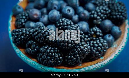 Fraises noires et myrtilles fraîches dans un bol en céramique sur fond bleu Banque D'Images