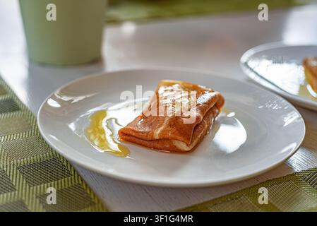 Une crêpe pliée arrosée de miel sucré repose sur une assiette en céramique. Banque D'Images