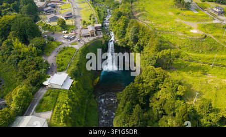 Vue aérienne d'une cascade dévalant dans un bassin profond entouré d'une forêt verte dense, de routes sinueuses et de petites constructions au Japon. Banque D'Images