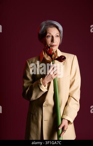 Sénior gracieuse en tenue élégante posant avec assurance avec une fleur à la main Banque D'Images