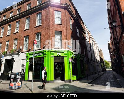 Dublin, Irlande – 22 mai 2026 : Magasin Paddy Power d’un vert éclatant à un coin de rue de Dublin avec un piéton, la lumière du soleil et une architecture en briques rouges. Banque D'Images